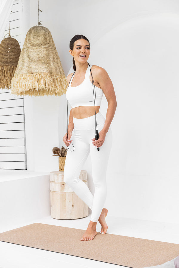 Woman standing on jute exercise mat holding a skipping rope.