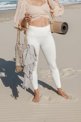 Woman on beach holding yoga mat and bag.