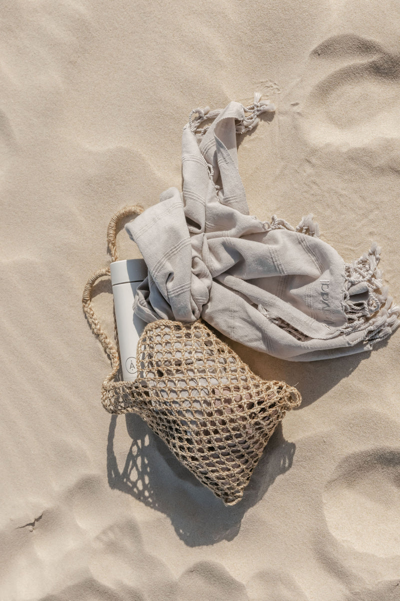 Jute bag on beach with towel and water bottle.