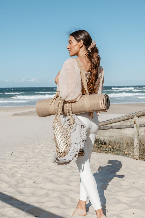 Woman on a beach carrying an exercise mat.