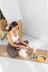 Woman sitting on a mat with water bottle, weights and bamboo sliders.